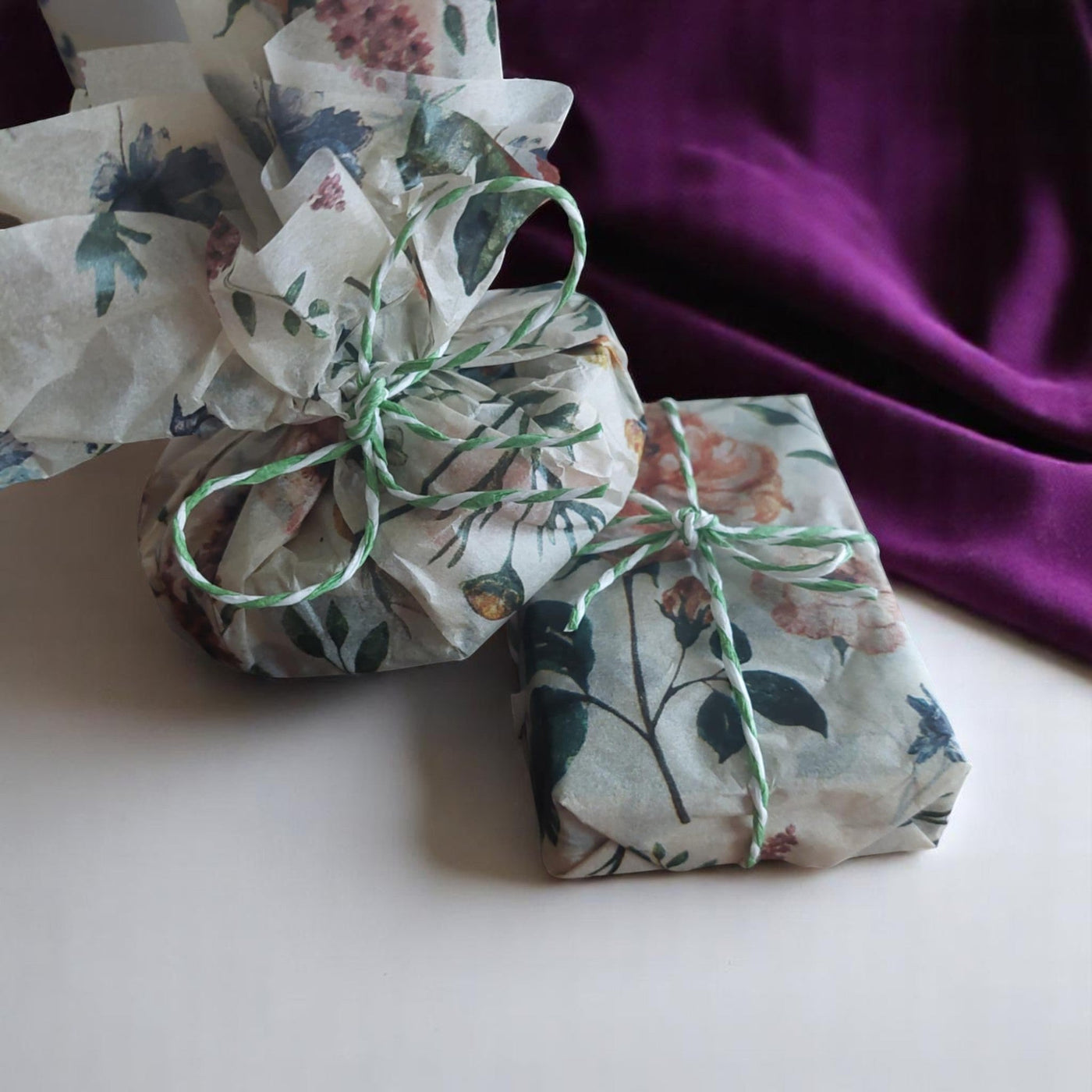 Artfully arranged, packages, wrapped in floral paper and tied with cording on a purple, velvet backcloth.
